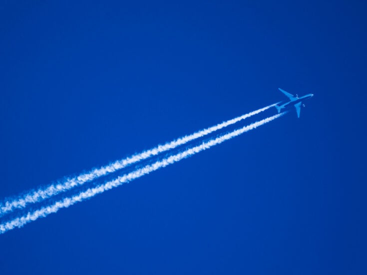 photo of aeroplane flying through blue skies with trails behind it. The UK Government has announced the first transatlantic net-zero flight using SAF sustainable aviation fuel