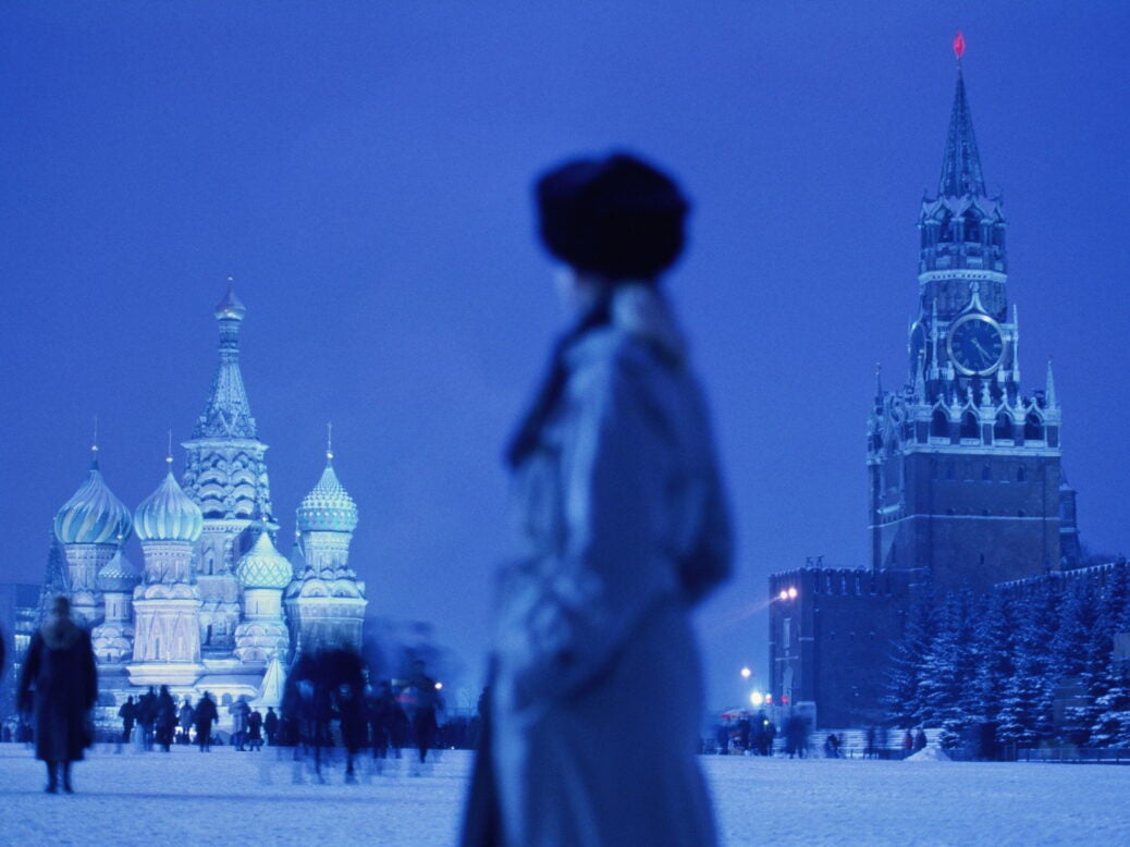 A figure standing in Red square, Moscow, Russia, at night. The Kremlin and St. Peter's Basilica are in the background